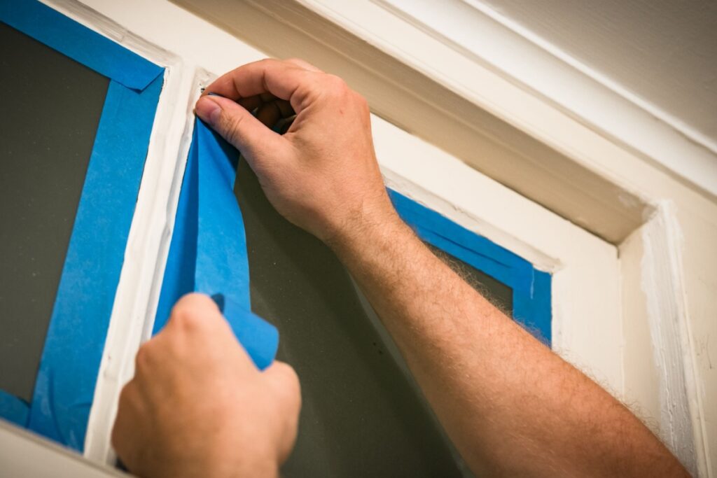 a professional painter's hands applying masking tape around window trim